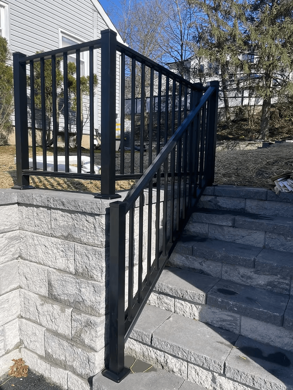 Black metal railing on stone steps in a residential landscape. Modern design and sturdy construction.