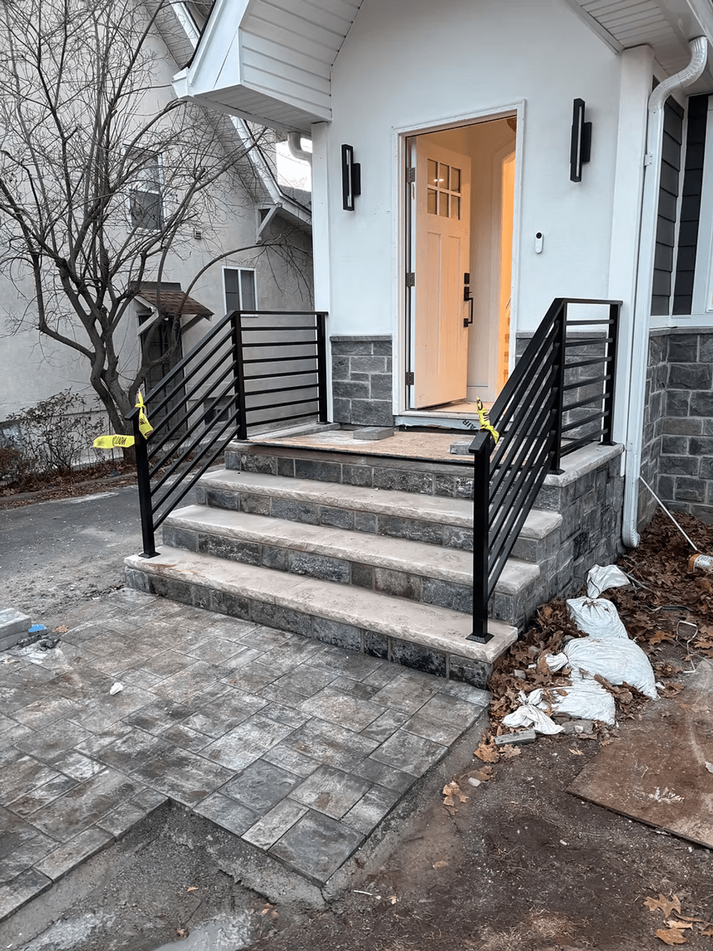 Modern black metal railing on steps leading to a front door with stonework and pavement.