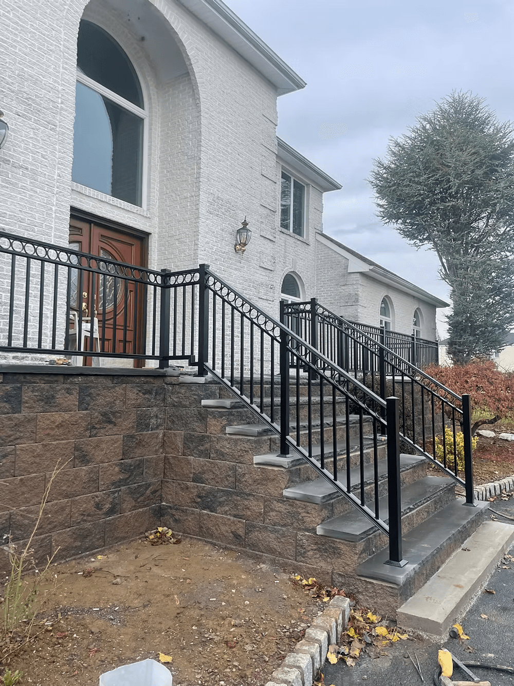 Black metal railing on a driveway stairs leading to a white house, featuring stone accents.