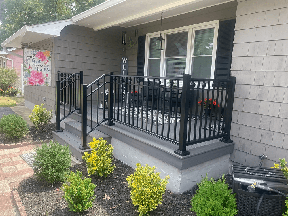 Modern porch with black railing, cozy seating area, and vibrant landscaping on a sunny day.