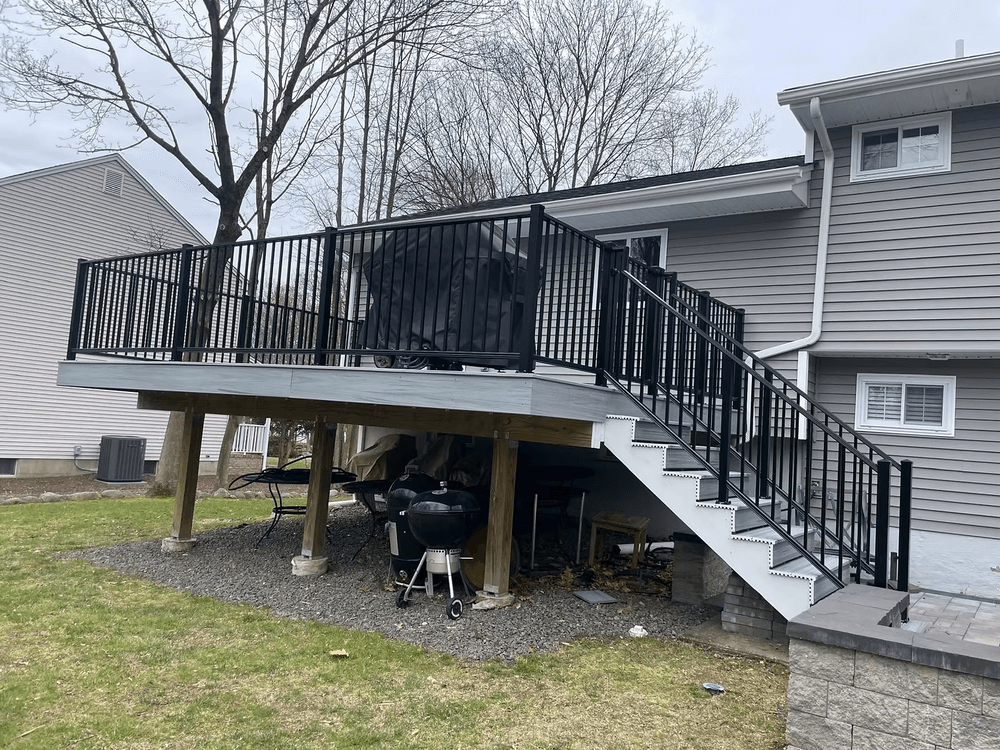 Modern outdoor deck with black railing and stairs, overlooking a backyard space.