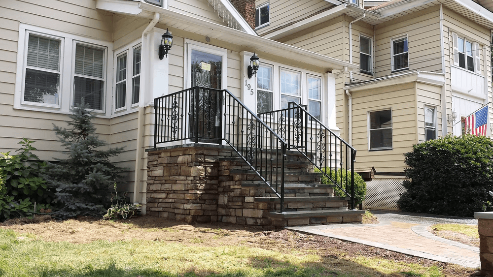 Modern home entrance with stone steps, black railing, and well-maintained landscaping.