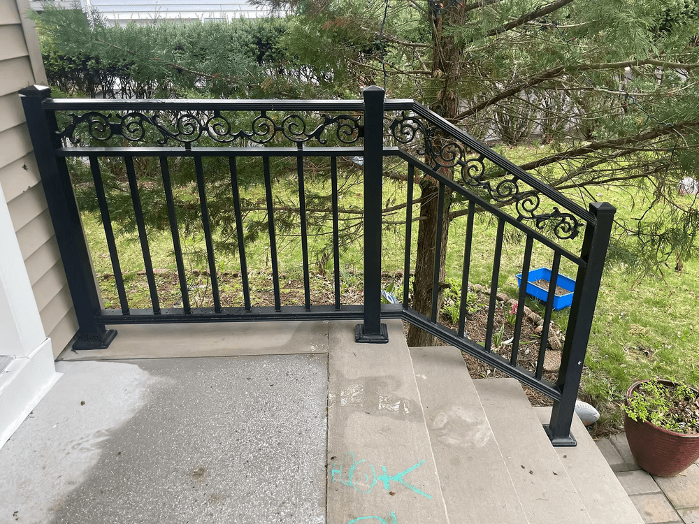 Black metal railing on a concrete porch with decorative scrollwork and a grassy background.