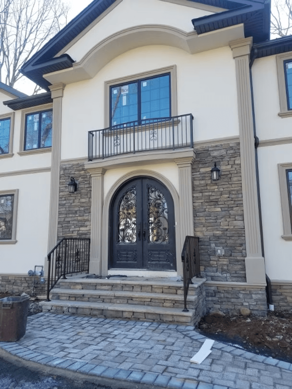 Elegant home entrance featuring decorative double doors, stone facade, and balcony.