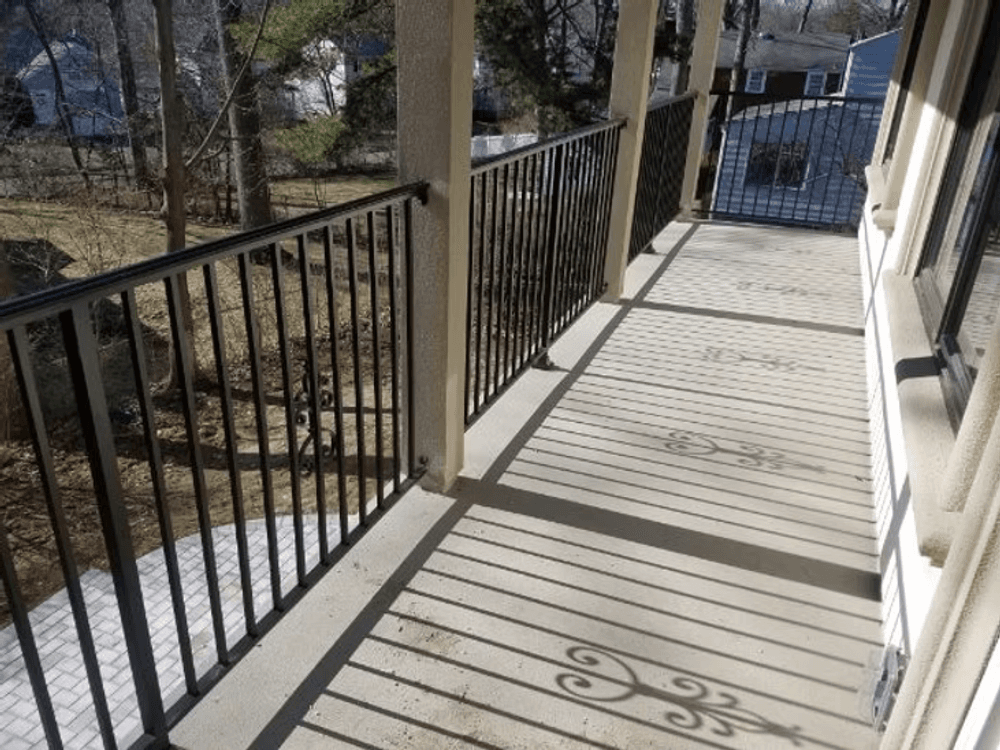 Spacious balcony with black railings casting shadows on concrete floor in a residential area.