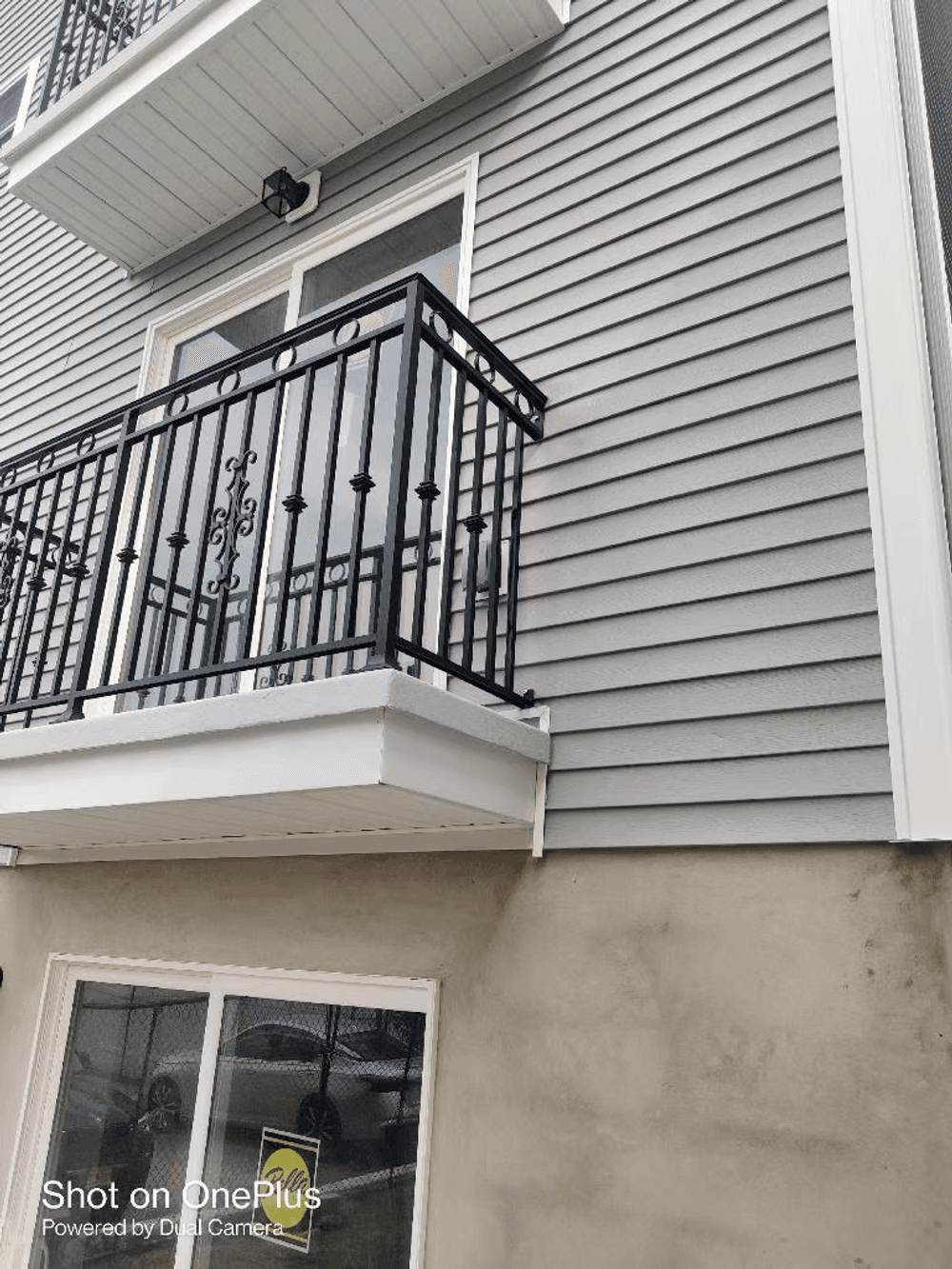 Modern building exterior featuring a balcony with ornate railing and gray siding.