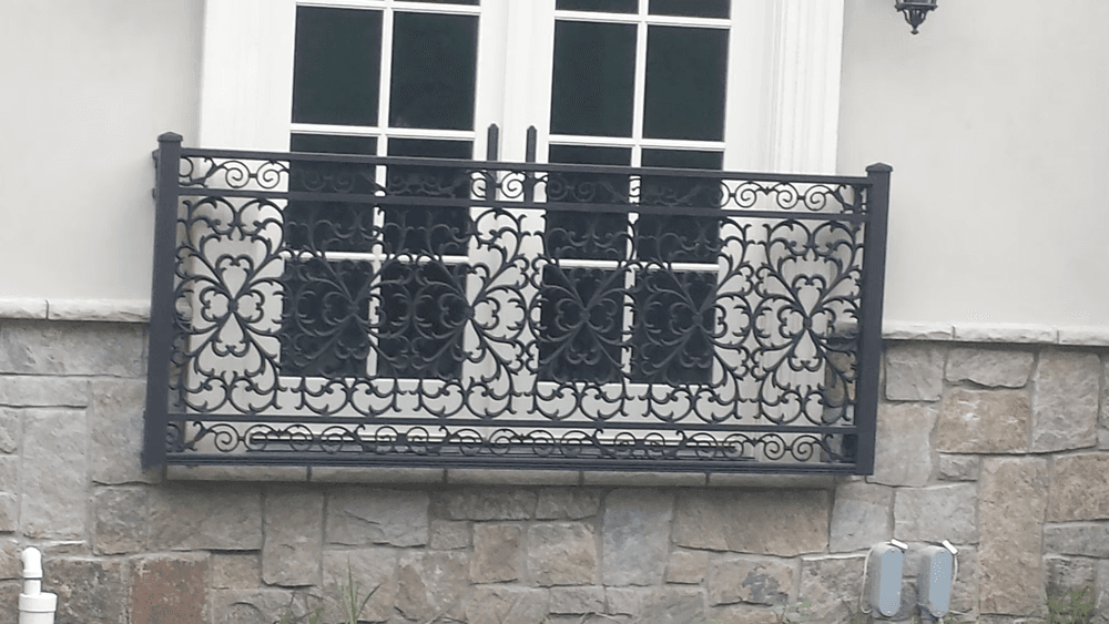 Wrought iron balcony railing with intricate floral design and stone wall background.