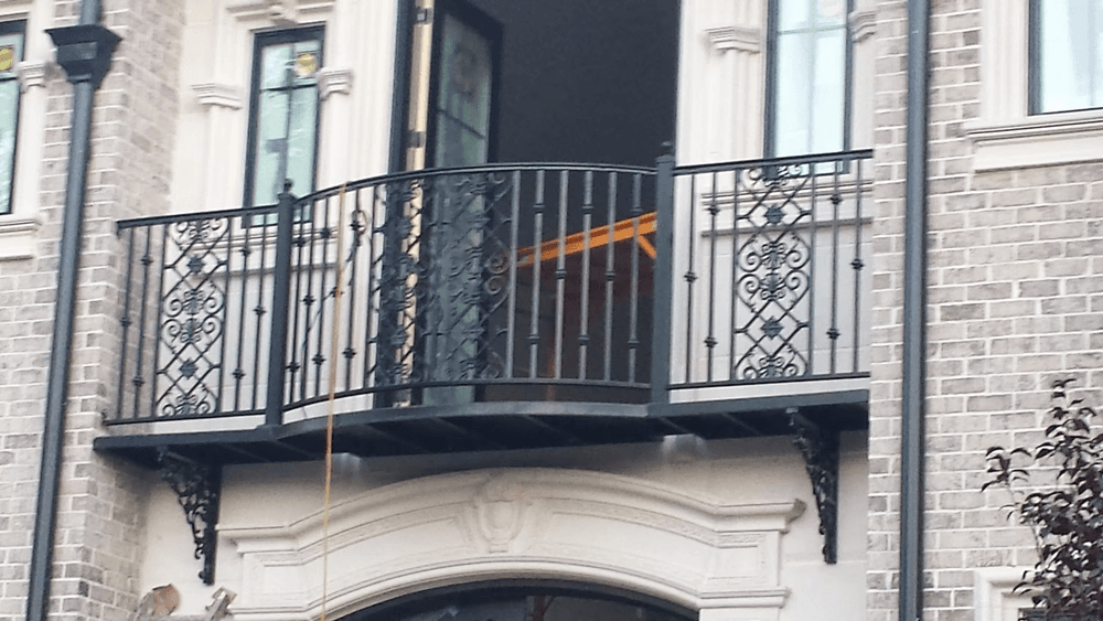 Intricate wrought iron balcony railing on an elegant brick building with large windows.