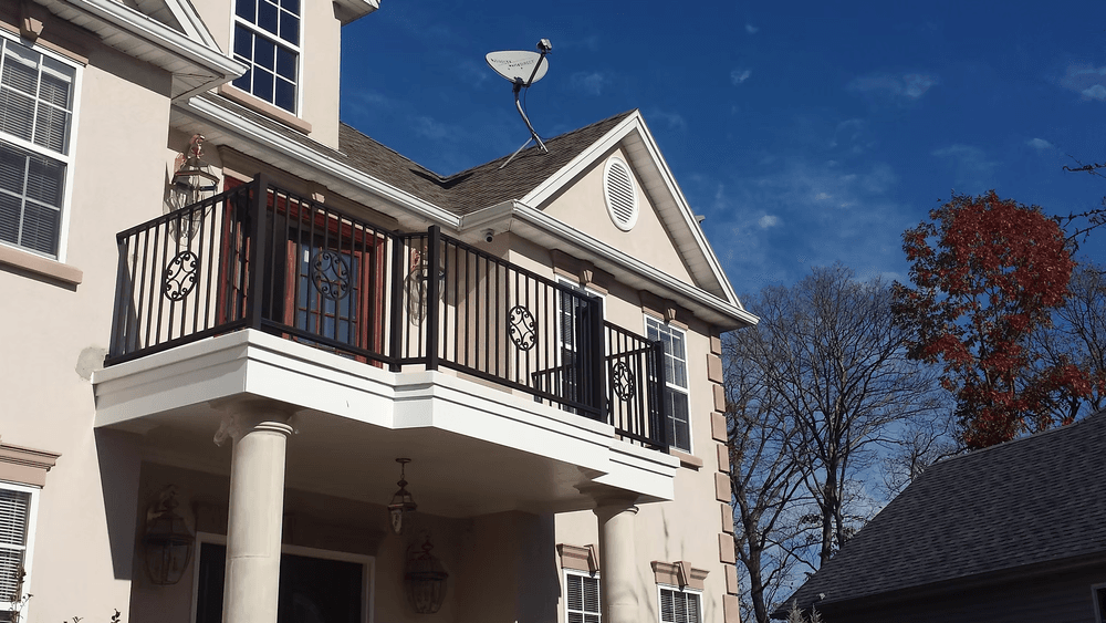 House exterior with balcony, satellite dish, and clear blue sky in background.