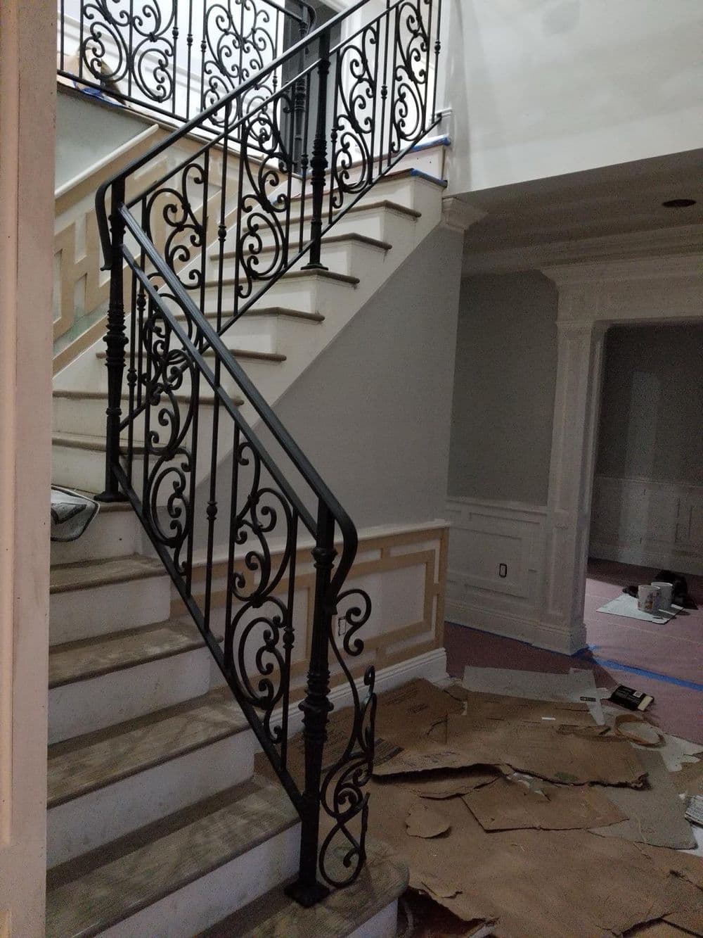 Elegant wrought iron staircase railing in a home under construction, with white walls and flooring.