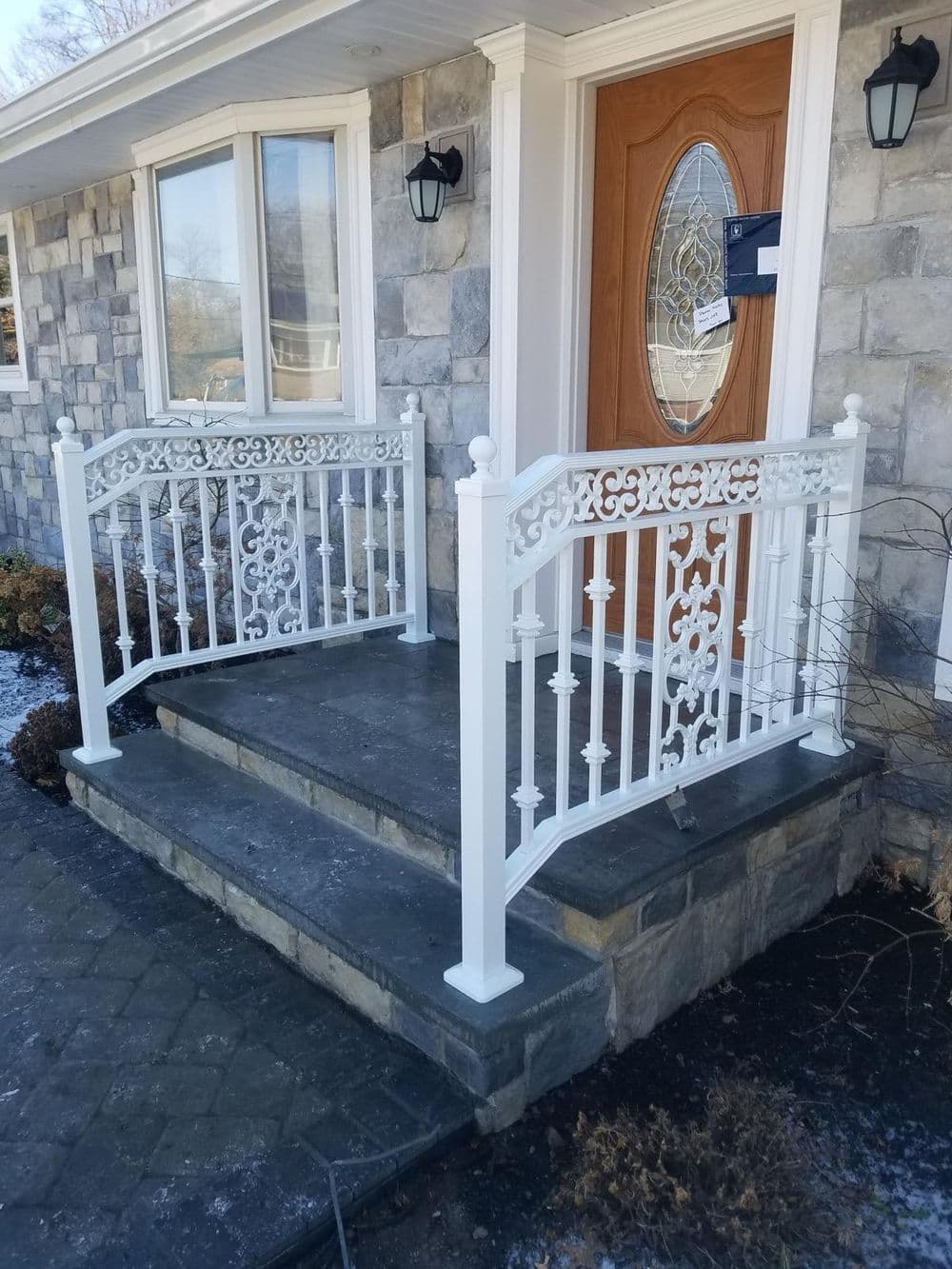 Decorative white metal railing at front entrance of stone-sided house with steps.