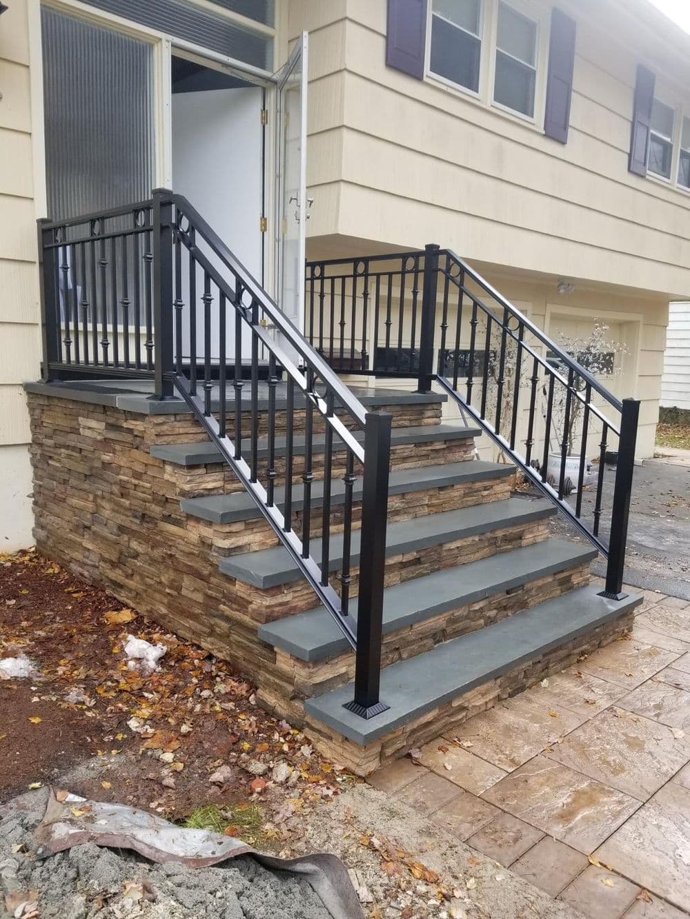 Modern stone and metal railing staircase leading to a home entrance, framed by natural surroundings.