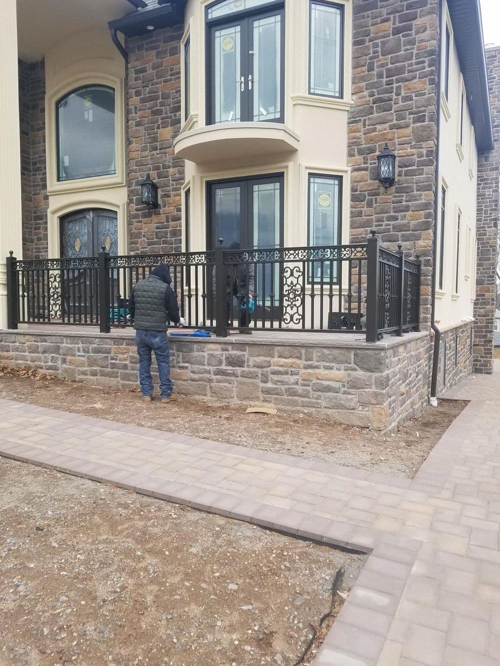 Worker installing black iron railing at a modern stone house with large windows.