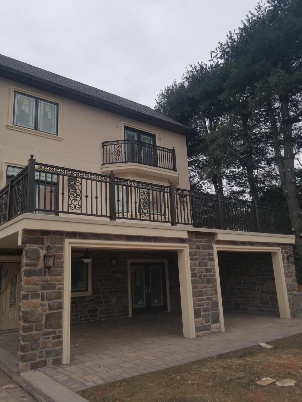 Modern two-story house with a stone facade and balcony surrounded by pine trees.