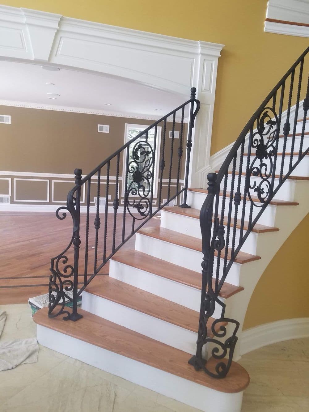 Elegant wooden staircase with ornate black iron railing in a stylish interior setting.