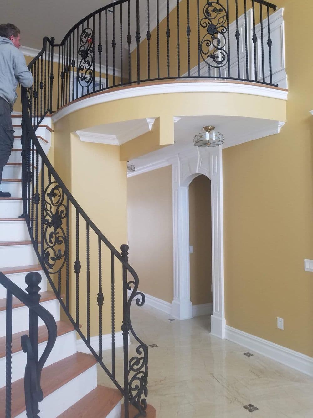 Elegant spiral staircase with ornate black railing in a well-lit foyer with golden walls.