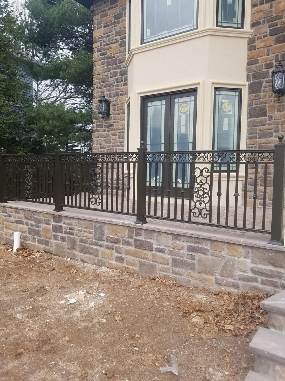 Decorative wrought iron railing on a stone patio of a modern home with large windows.