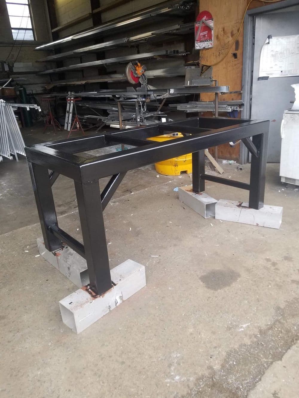 Metalworking table with a sturdy frame, elevated on concrete blocks in a workshop setting.