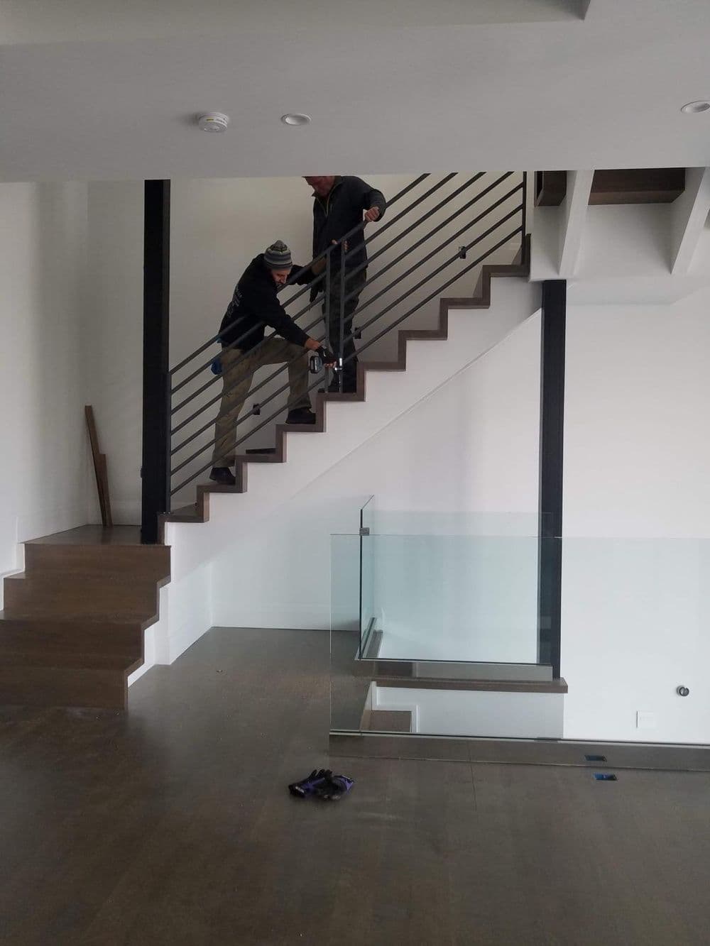 Workers installing railing on modern staircase in newly constructed home interior.