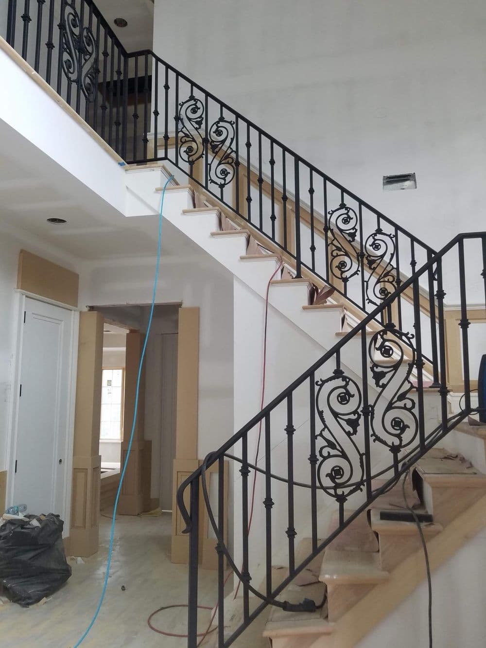 Elegant staircase with wrought iron railings in a partially finished home interior.