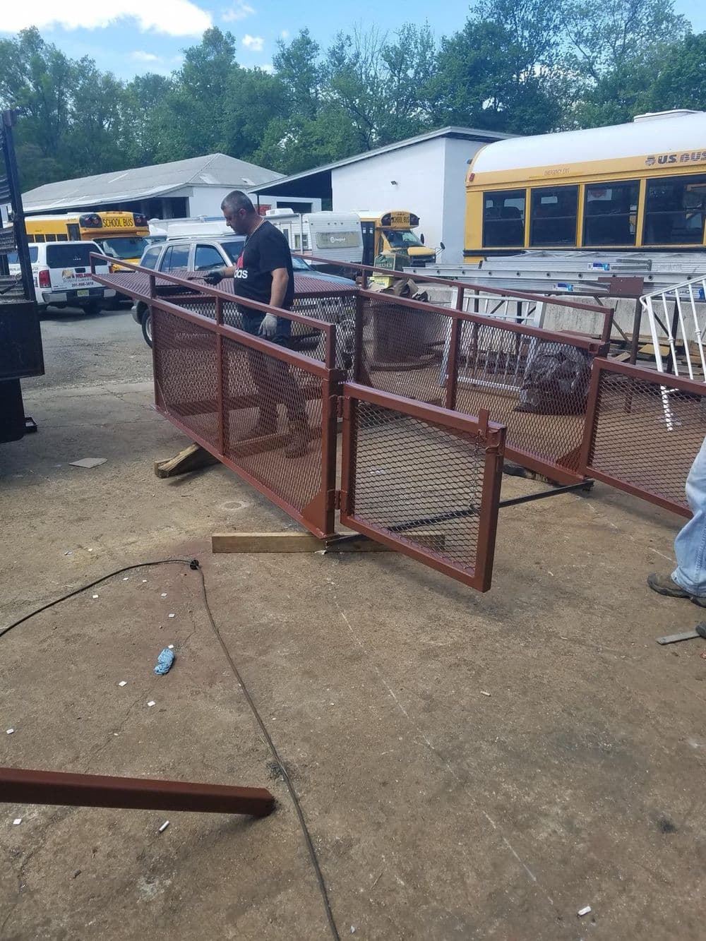 Man assembling a metal gate with mesh panels in a workshop surrounded by vehicles.