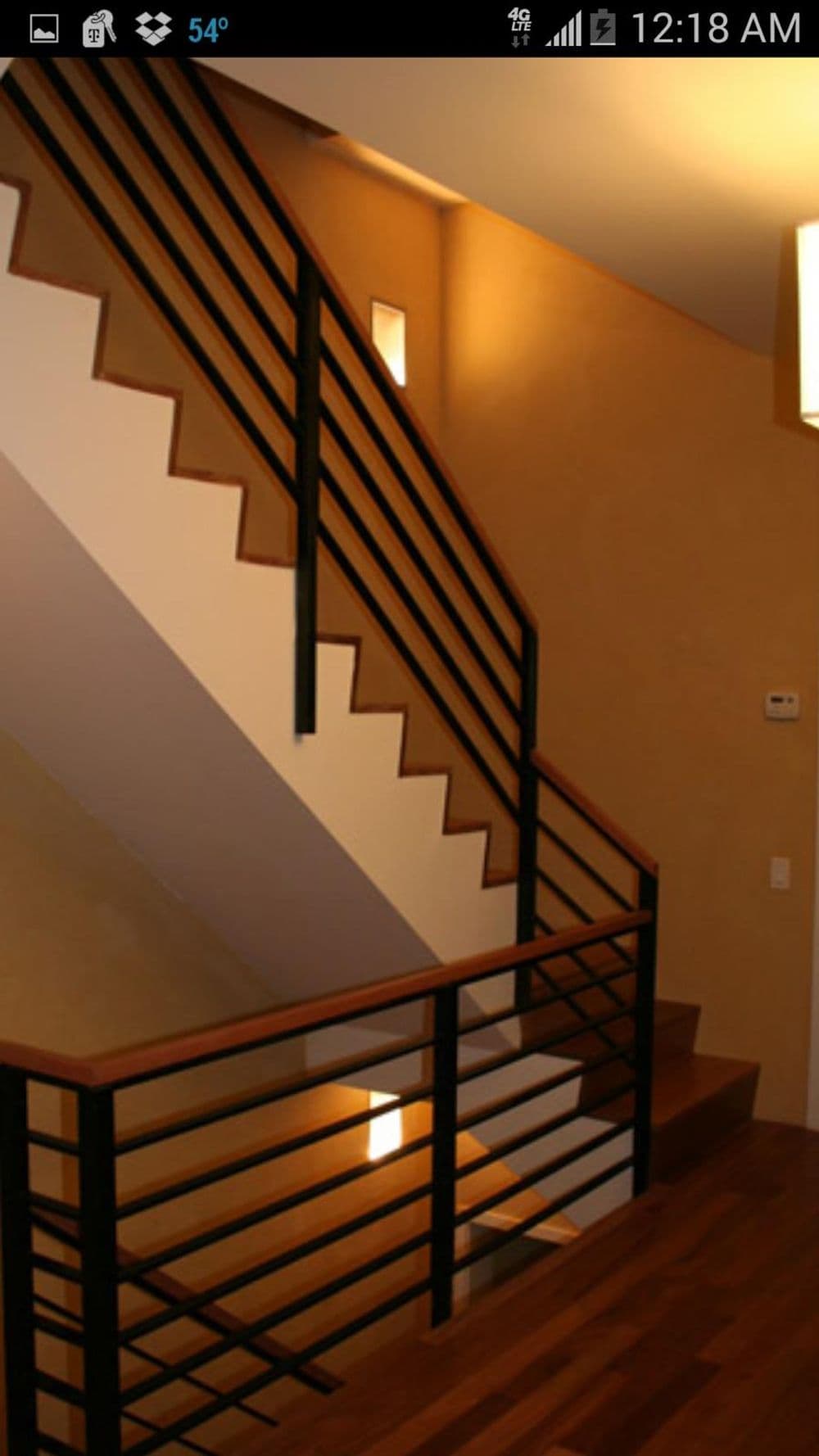 Modern staircase with wooden steps, black railing, and warm wall lighting.