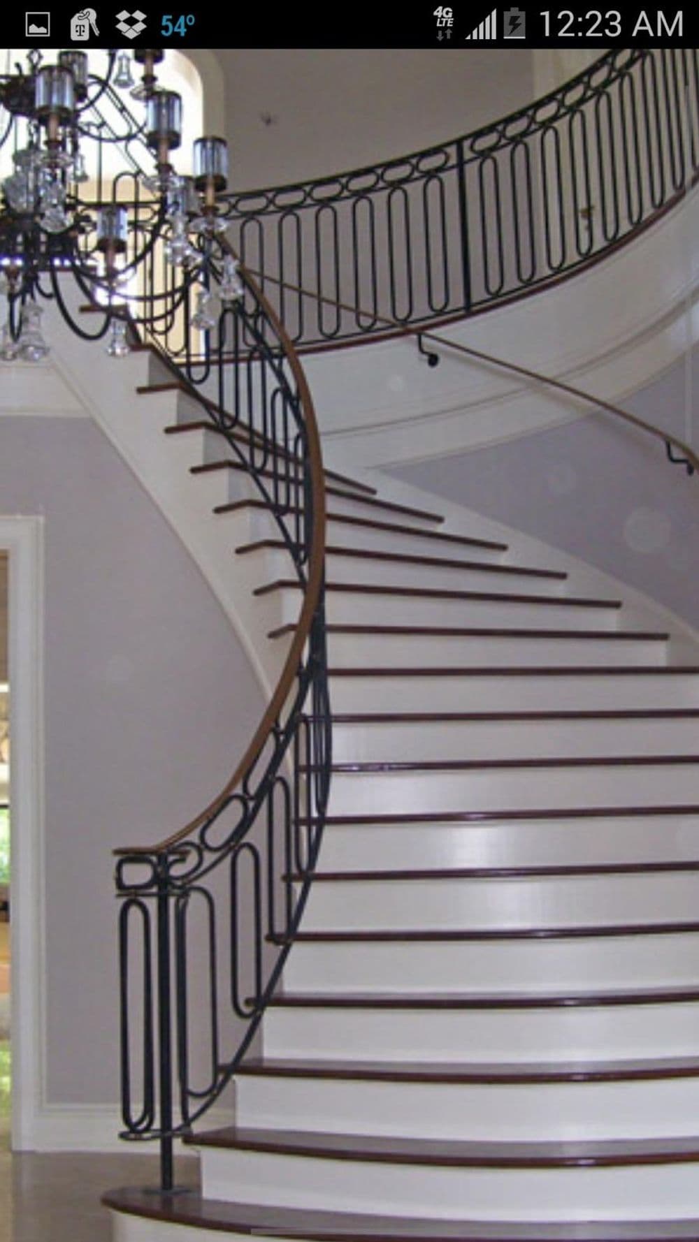 Curved wooden staircase with elegant black railings and chandelier in a modern interior.