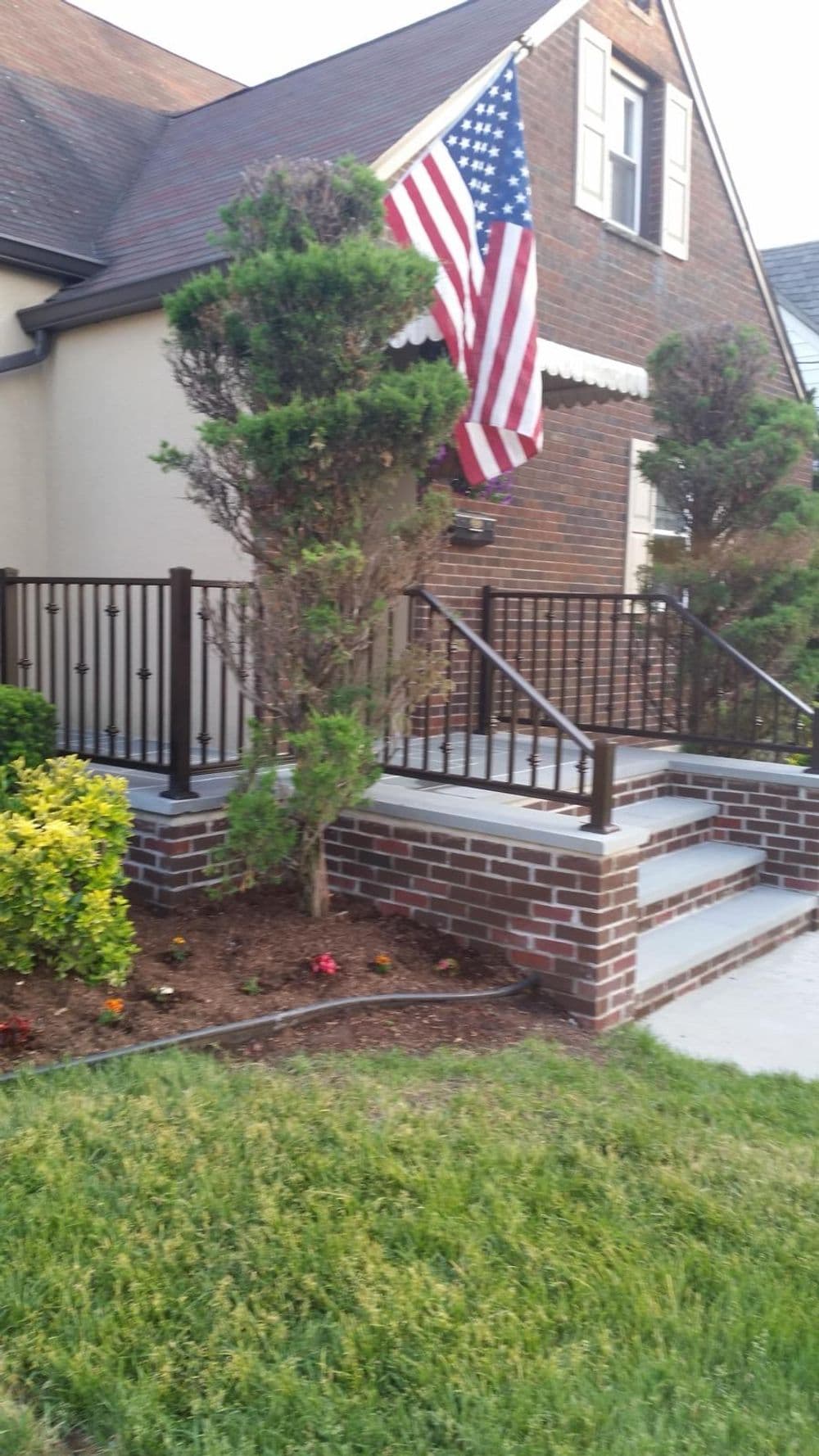 American flag decorates a brick-front home with landscaped gardens and a ramp.