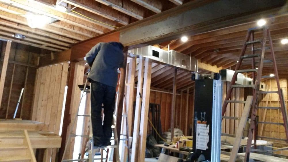Construction worker on ladder installing beams in unfinished building interior.