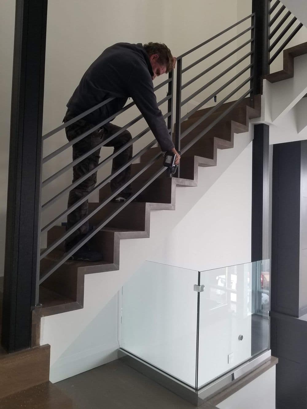 Man installing a modern metal railing on a staircase with glass detailing.
