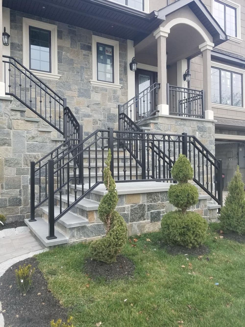 Elegant stone staircase with black railings and manicured shrubs leading to a modern home entrance.