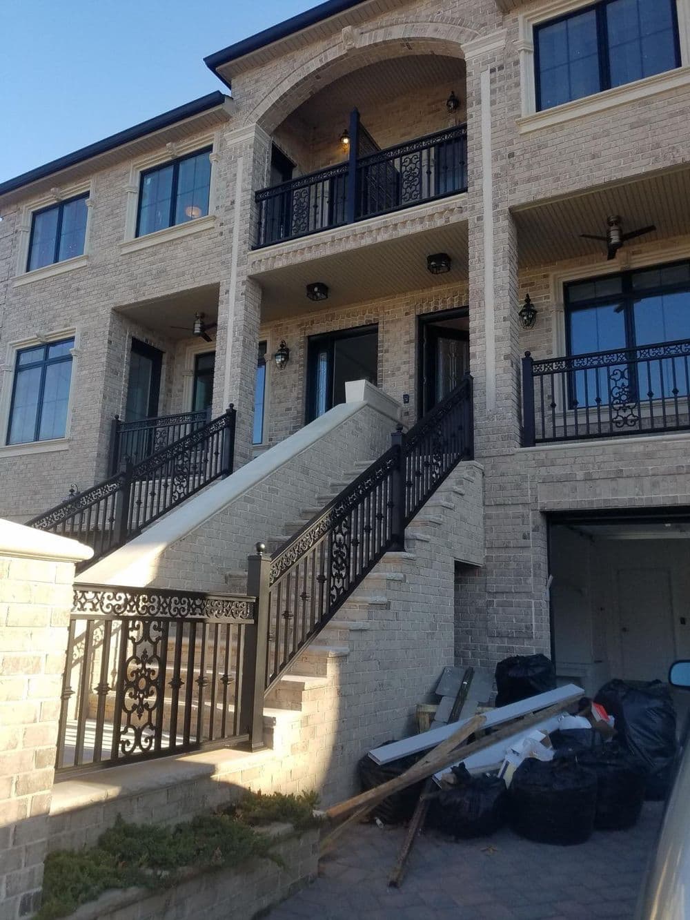 Three-story brick building with elegant balconies, black railings, and construction debris in front.