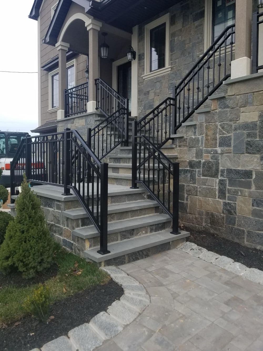 Modern stone staircase with black railings leading to an elegant house entrance.