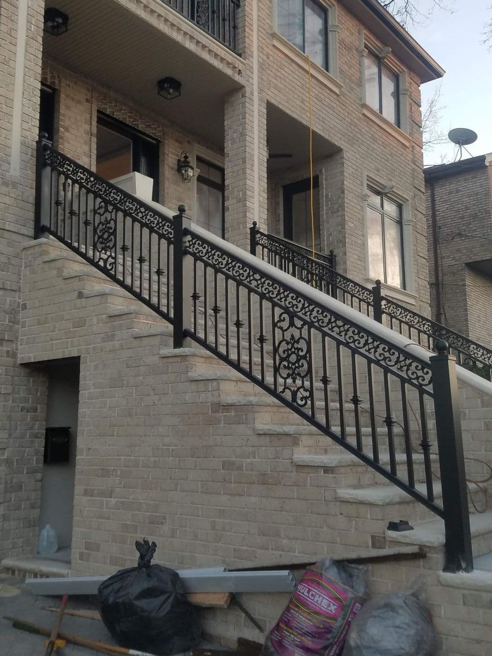 Elegant black wrought iron railing on brick staircase leading to a modern home entrance.
