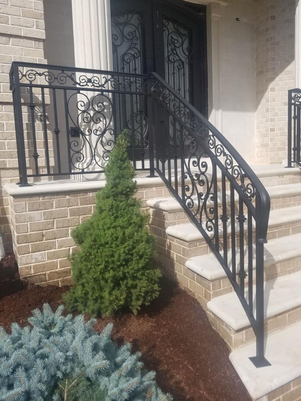 Elegant wrought iron railing on stone steps with landscaped greenery near the entrance.