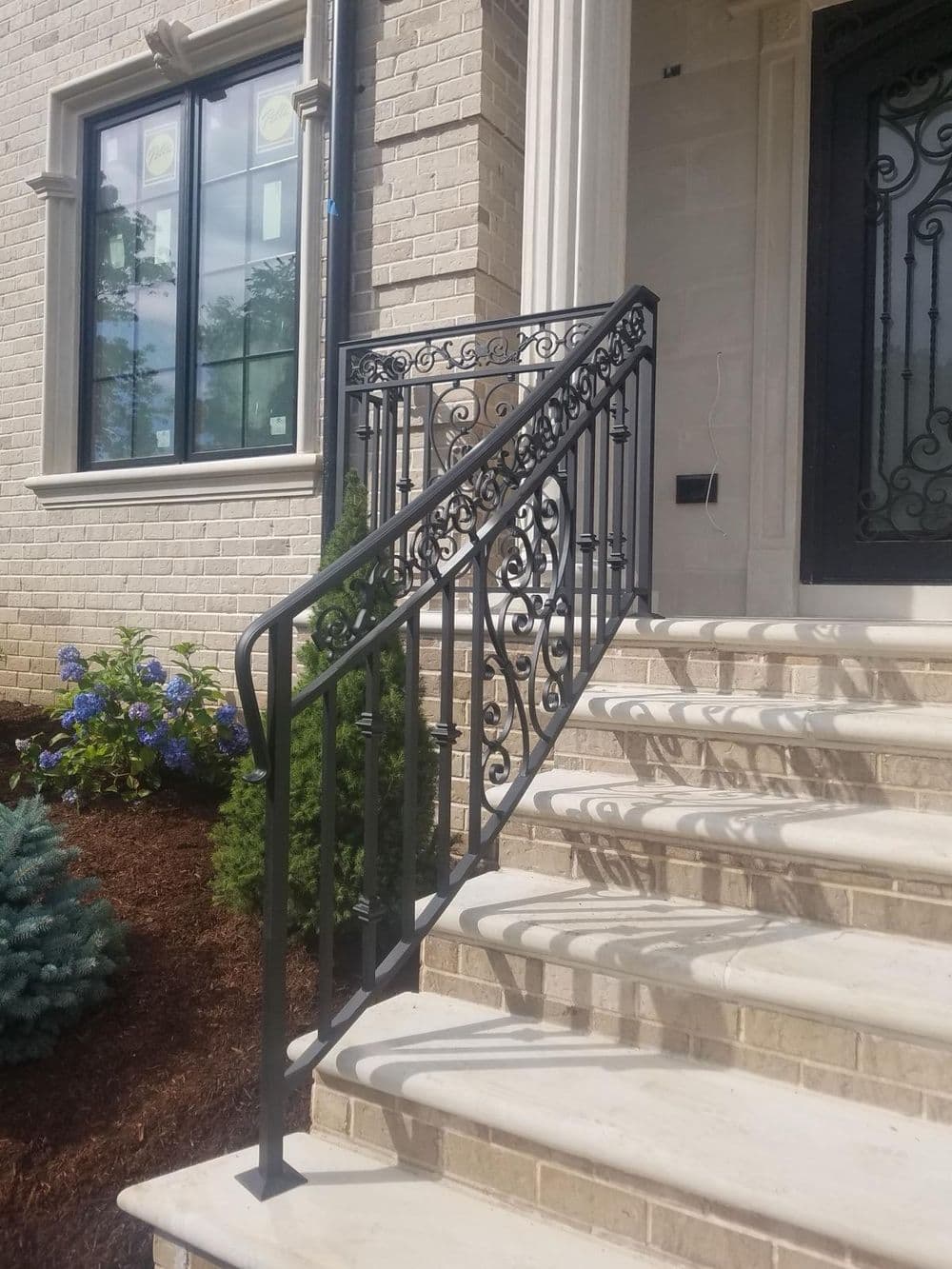 Elegant black wrought iron railing on a stone staircase beside a modern home entrance.