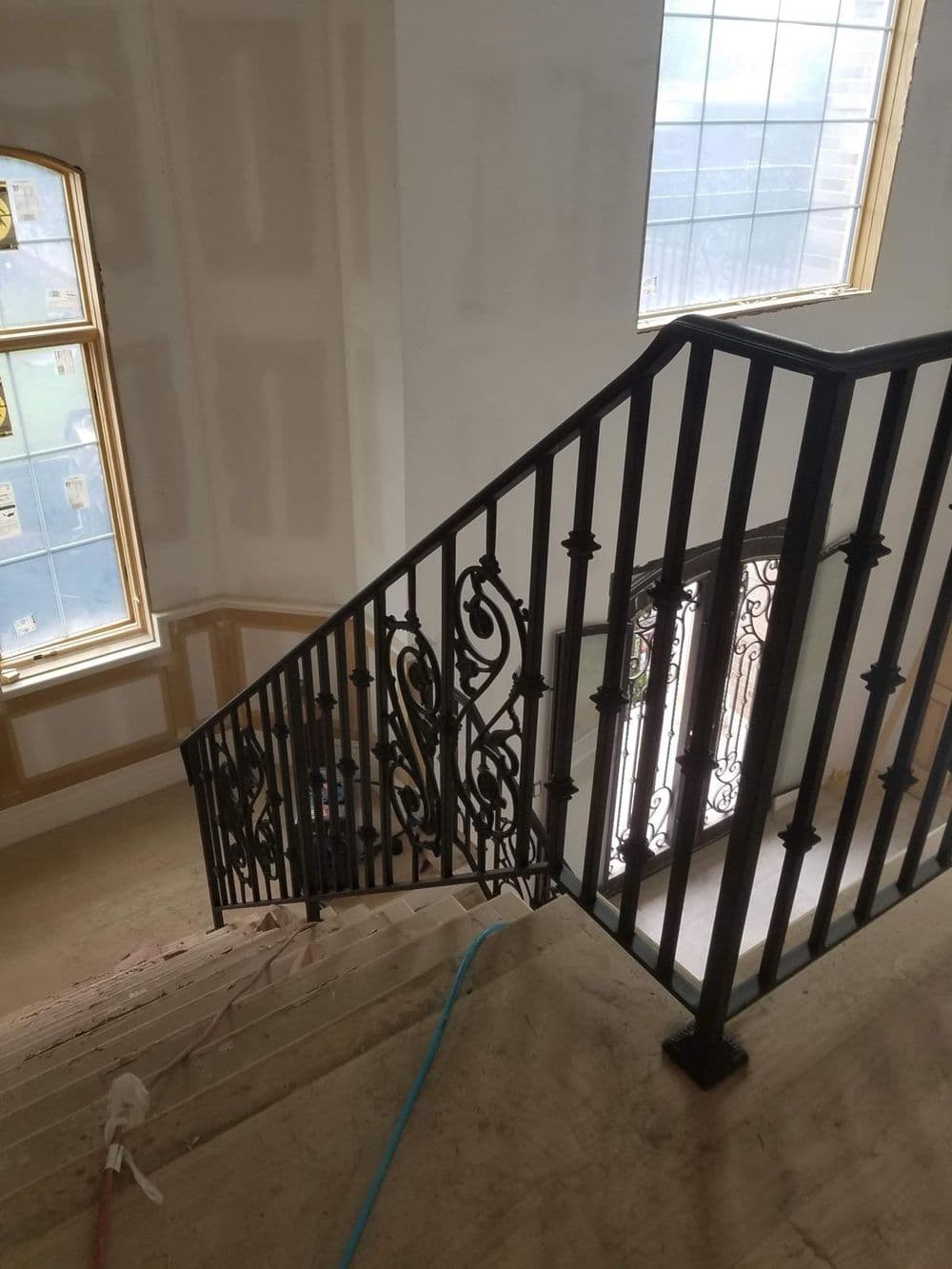 Elegant wrought iron staircase railing leading to a light-filled entryway in a home under construction.