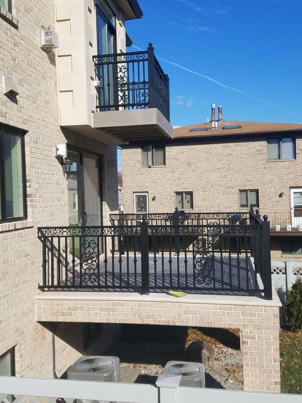 Two balconies with black wrought iron railings, overlooking a landscaped area and blue sky.