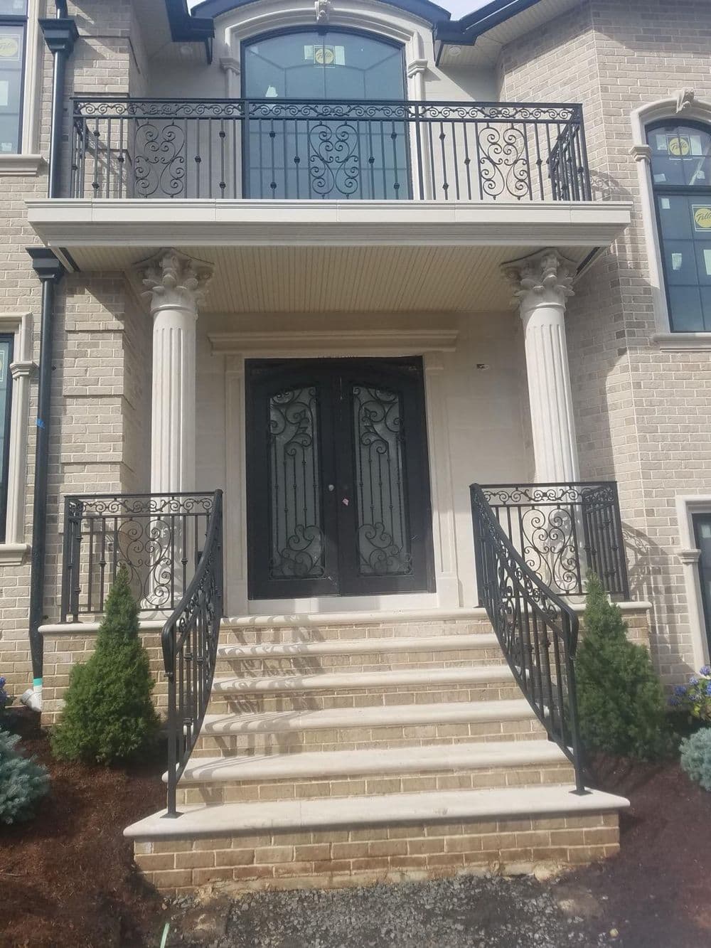 Elegant brick home entrance with double doors, wrought iron railing, and stone steps.
