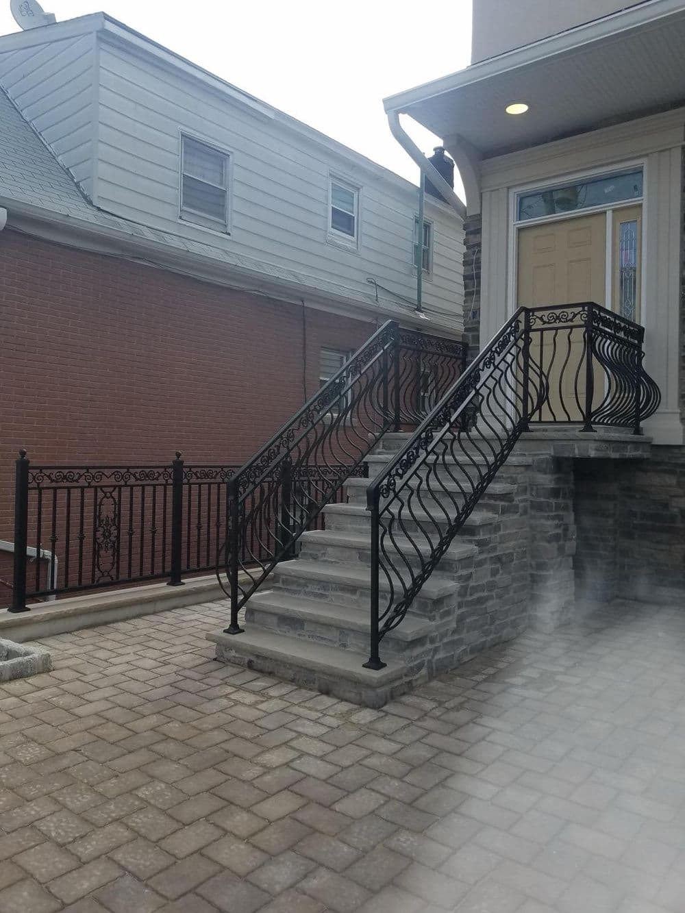 Black wrought iron railing on stone steps leading to a home's entrance with brick siding.