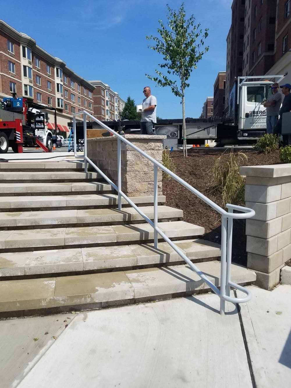 Railing on stairs with landscaping and workers at a construction site in urban setting.