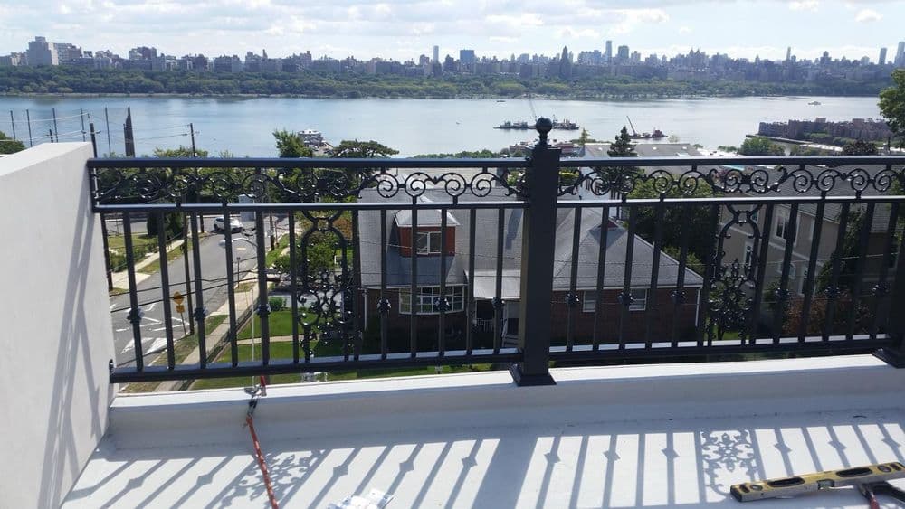 Rooftop balcony with iron railing overlooking river and city skyline in the background.