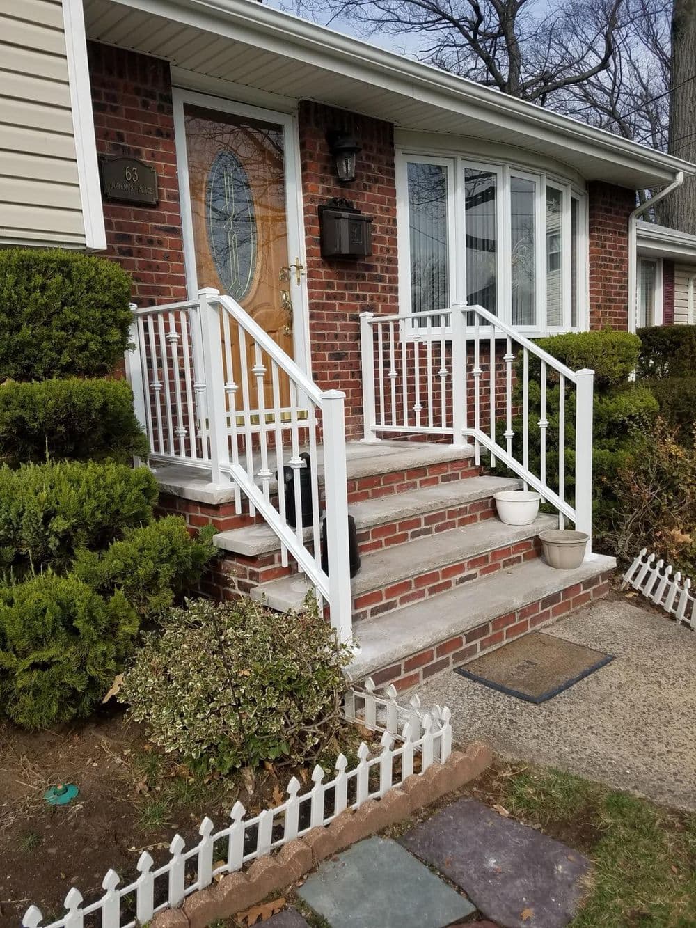Charming red brick house entrance with white railing and landscaped garden.