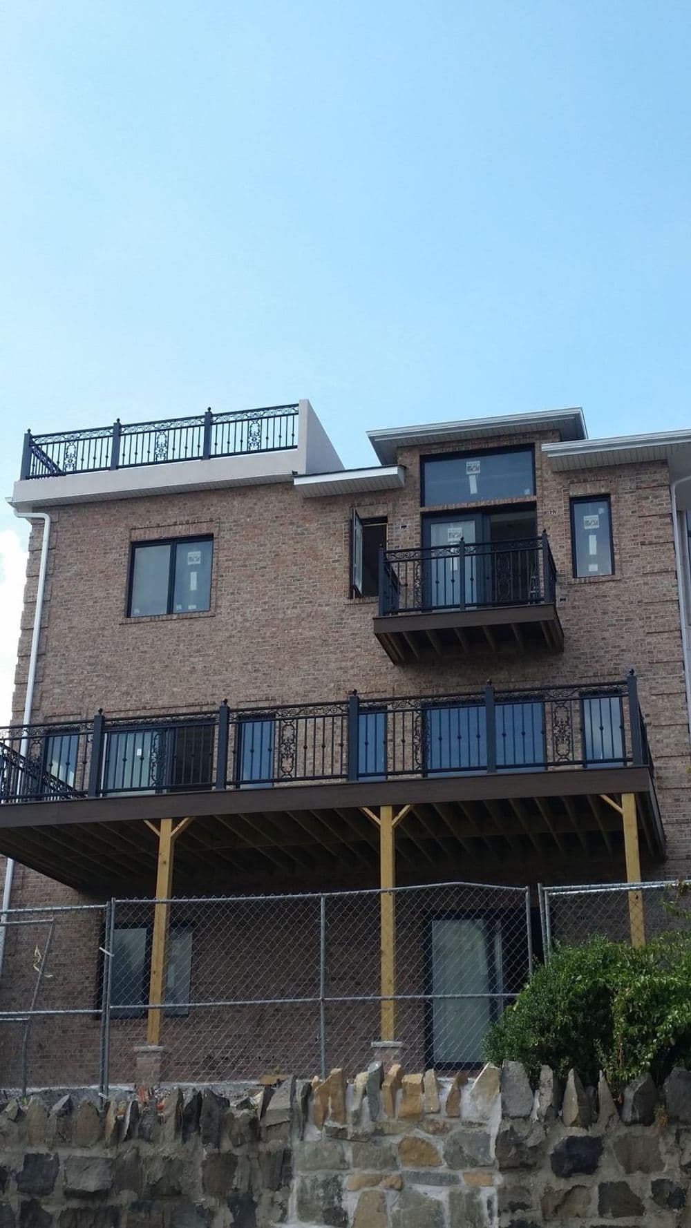 Modern two-story brick house with a balcony, surrounded by a fenced yard and clear sky.