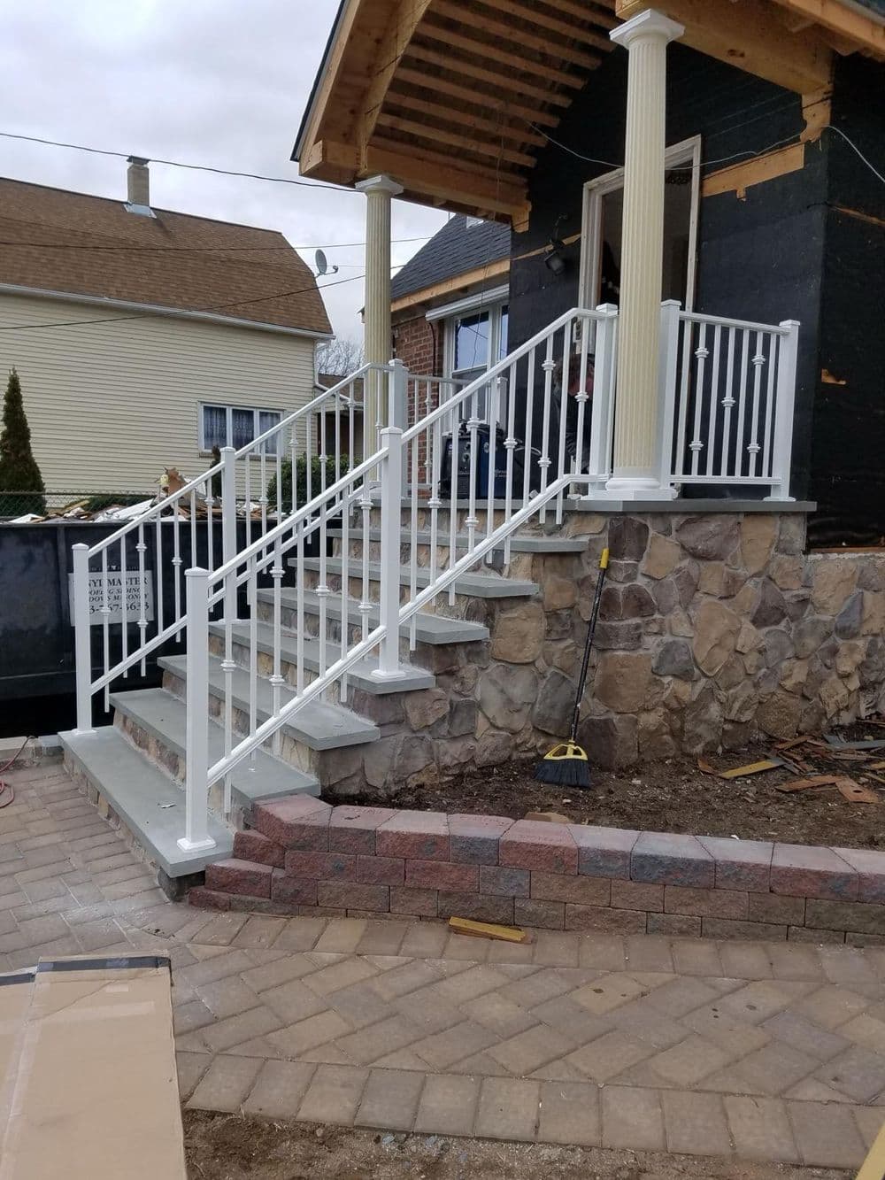 White railing on a stone staircase leading to a house under construction.