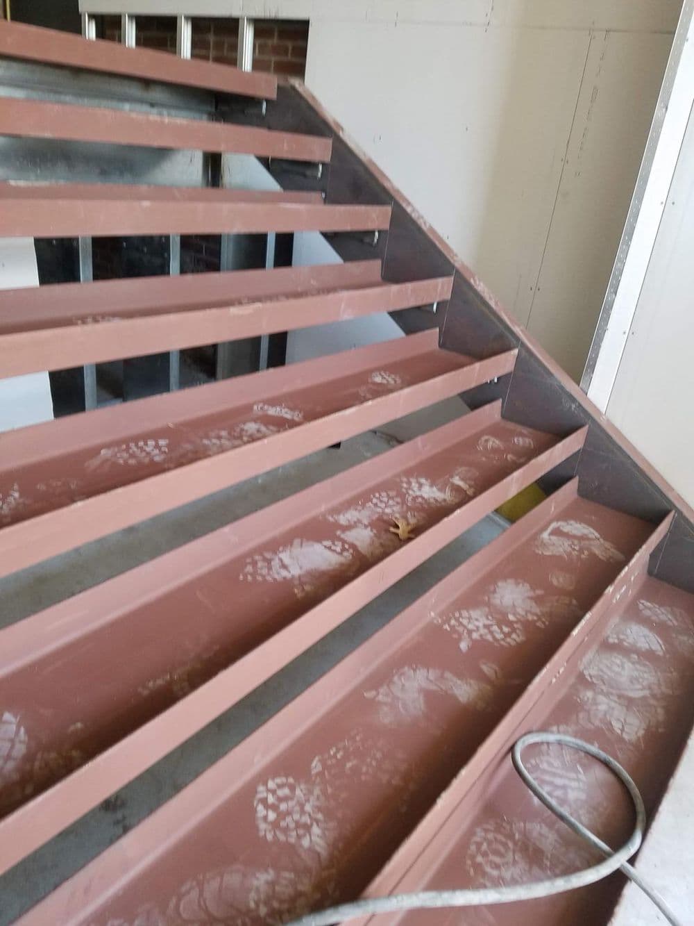 Metal staircase framework under construction with visible footprints and unfinished walls.