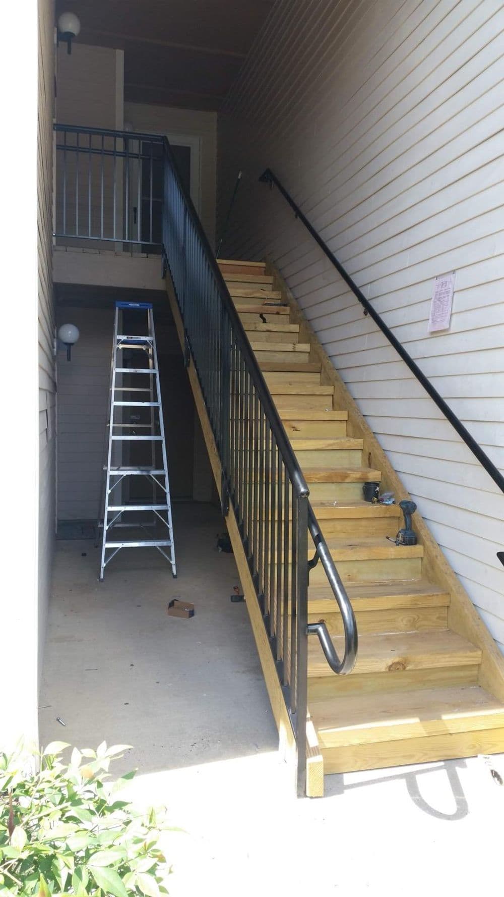 Exterior view of wooden stairs with railings and a ladder beside them.