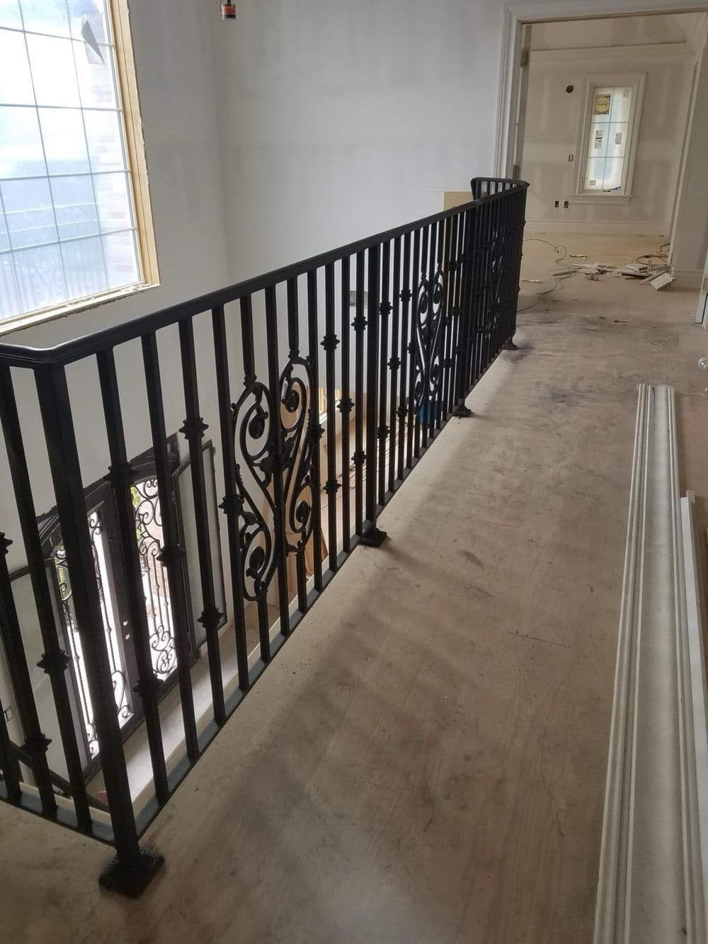 Black wrought iron railing on a second-floor hallway overlooking a construction site.
