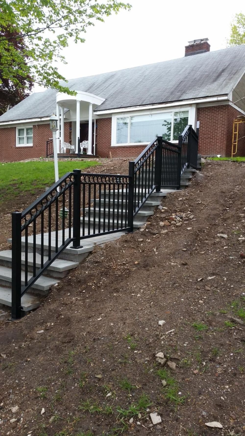 Black wrought iron railing on concrete steps leading to a residential home in a hillside setting.