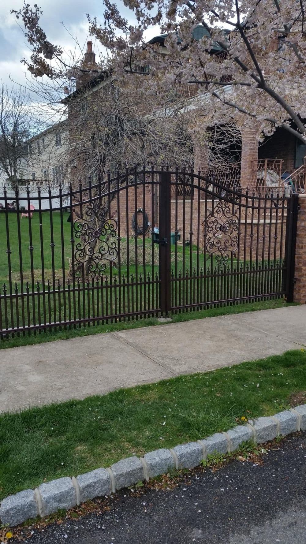 Decorative wrought iron gate leading to a well-manicured garden with cherry blossoms.